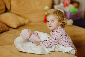 Adorable cute little toddler girl playing with doll. Happy healthy baby child having fun with role...