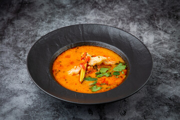 spicy tom yum in a black plate with greens, side view