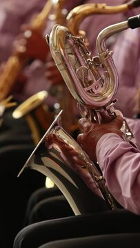 vertical video, close up hands of hispanic, latino male musician playing the baritone saxophone during a concert