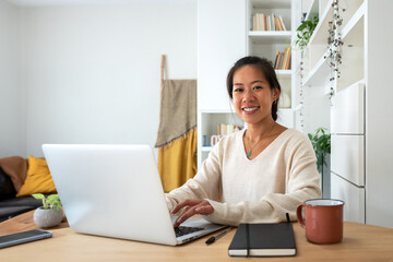 Asian female entrepreneur working using laptop looking at camera. Smiling Chinese woman working...