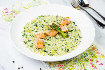 rice porridge with artichoke, red fish and herbs in a white plate, side view