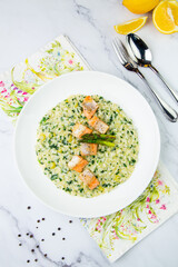 rice porridge with artichoke, red fish and herbs in a white plate, top view