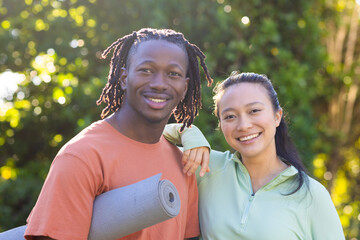 Portrait of happy diverse couple holding yoga mat smiling in sunny garden