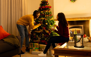 Happy diverse couple decorating christmas tree at home and talking