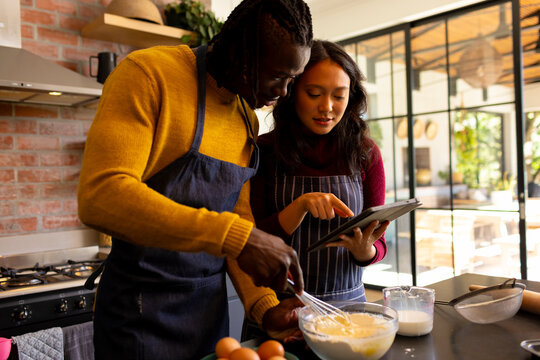 Happy diverse couple baking mixing dough and suing tablet in kitchen - Powered by Adobe
