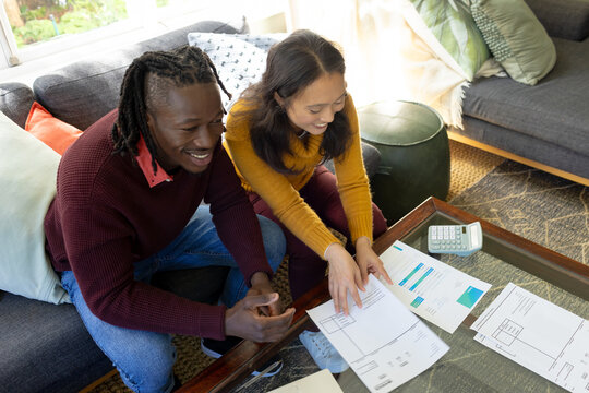 Happy diverse couple sitting on couch discussing bills and domestic finances in living room