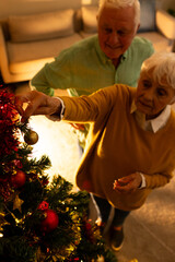 Happy caucasian senior couple decorating christmas tree in living room at home
