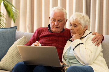 Caucasian senior couple holding pills and having video call in sunny living room