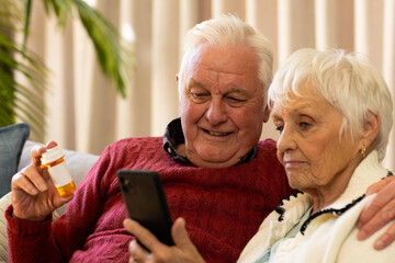 Caucasian senior couple holding pills and having video call in sunny living room - Powered by Adobe