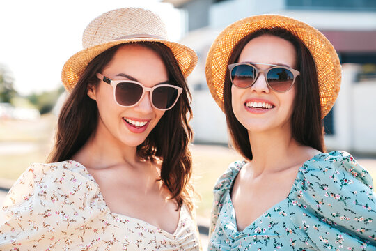 Two young beautiful smiling hipster female in trendy summer dresses  clothes. Sexy carefree women posing in the street. Positive models having fun at sunny day. Going crazy. In sunglasses and hat