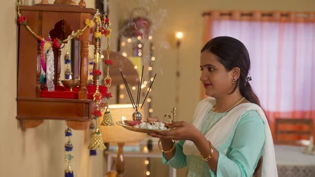 young Indian girl offering mangal aarthi with incense sticks to god near mandapam at home during diwali festival celebration - concept of traditional religious custom, fragrance and spirituality