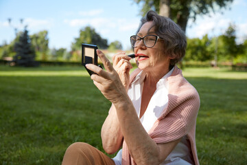 Senior woman applying lipstick doing makeup for charming smile