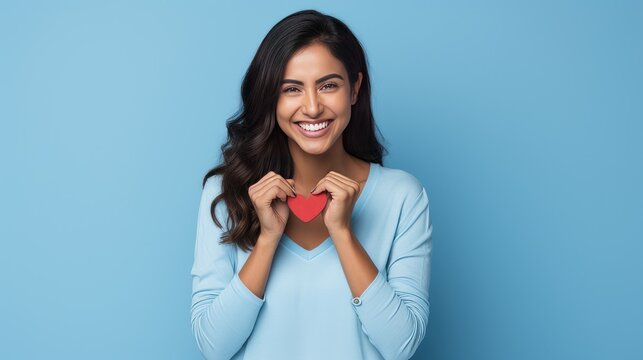 Hispanic woman standing over blue background smiling lovingly and making heart symbol shape with hands. romantic concept. I love you. Valentine's day 