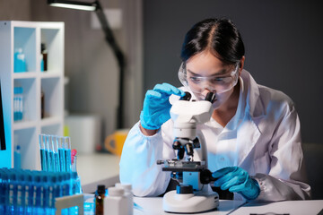 Asian female scientist looking under microscope, analyzes petri dish sample. specialists working on...