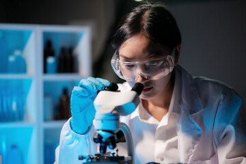Asian female scientist looking under microscope, analyzes petri dish sample. specialists working on medicine, biotechnology research in advanced pharmacy lab, Medical development laboratory.