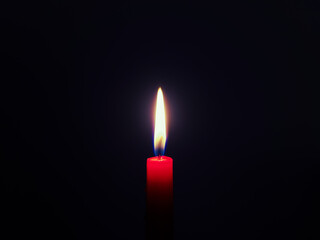 Burning red candle in front of a very dark blue background
