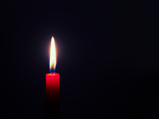 Burning red candle in front of a very dark blue background
