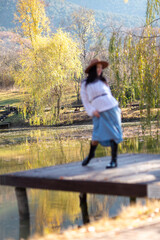 Fototapeta na wymiar Autumn lake woman. She stands by a pond on a wooden pier in autumn and admires nature. The concept of tourism, weekends outside the city.
