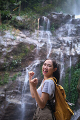 Portrait of female tourist making winner yes gesture celebrating success at beautiful tropical waterfall