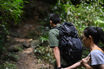 Active young couple with backpack trekking in forest, exploring nature. Traveling, trekking and adventure concept