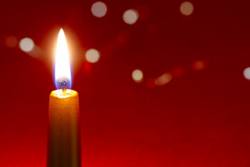 Burning golden candle on red background with glittering bokeh lights, christmas background, copy space