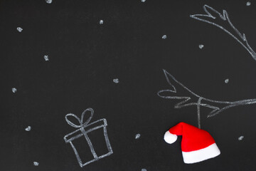 Gift and reindeer antlers drawn with chalk on blackboard with Santa Claus hat, creative concept...