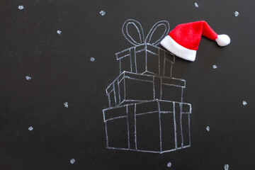Stack of gifts drawn with chalk on blackboard with Santa Claus hat, creative concept christmas...