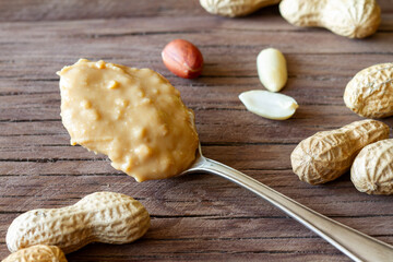 Obraz na płótnie Canvas Spoon of peanut butter and peanuts on wooden boards, healthy nutritious snack