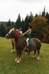 Young women ride horses in national Ukrainian dresses in the Carpathian mountains. Photo session with horses in the mountains. Ukrainian culture concept