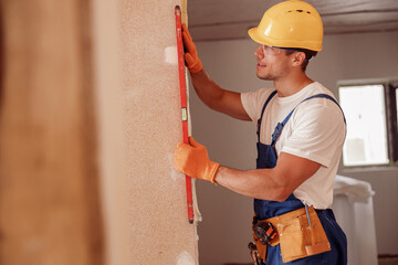 Joyful male builder measuring wall in house