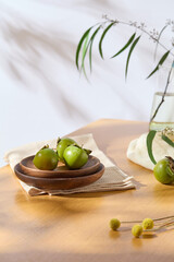 A wooden dish containing green persimmons placed on folded towel. Branch of green leaves decorated. Autumn holiday concept
