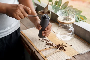  Asian man grinding coffee beans with grinder to easily drip black coffee at home, saving time and getting coffee that has a special aroma and taste. Soft and selective focus.  © Aoy_Charin