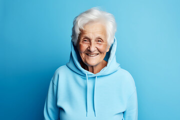 Smiling senior woman posing in blue hoodie on blue background - Powered by Adobe