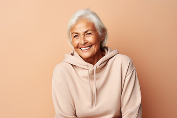 Fototapeta premium Smiling senior woman posing in beige hoodie on peach background