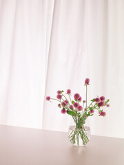 Pink Oleander Flowers in a Glass Vase, Swirling Curtain in the Background.	