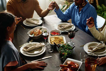 Hands of religious African American family members during Thanksgiving pray by served table with...