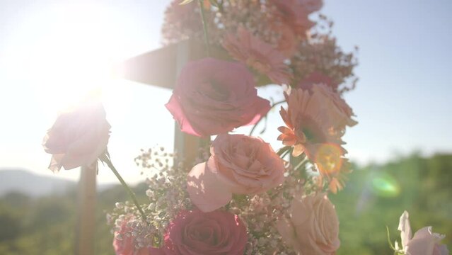 pink roses on golden wedding arch, dolly shot, sun flare shining, outdoor ceremony