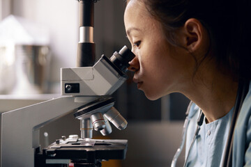 Asian lab assistant uses microscope working with material sample at table in laboratory