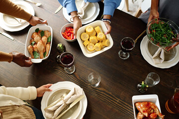Above angle of hands of family members putting homemade food on table while preparing for festive dinner on Thanksgiving day