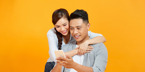 Image of excited surprised loving couple isolated over yellow background using mobile phone. - obrazy, fototapety, plakaty