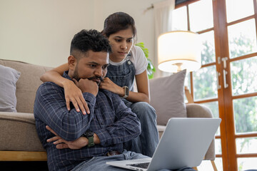 Indian couple sitting together indoors in the home house, calculating finances at home, looking seriously in documents bills payment online - obrazy, fototapety, plakaty