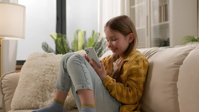 Happy smiling caucasian kid girl child schoolgirl typing message on smartphone at home couch browsing social media chatting using learning application for education play virtual game on mobile phone - Powered by Adobe