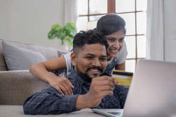 Happy indian couple with bank card and laptop at home, Young caucasian couple smiling happy using...