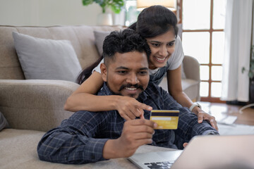 Happy indian couple with bank card and laptop at home, Young caucasian couple smiling happy using...