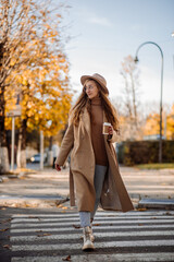 A beautiful adult woman in a coat and hat walks on the road in the middle of the city in the autumn season