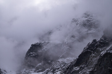 Captured in Rysy, this shot reveals the majesty of a snow-draped mountain peak, partially hidden by swirling mists. The rugged, icy surface and the ethereal fog present a stark, haunting beauty.