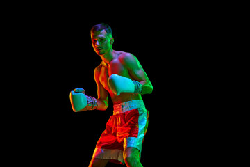 Confident shirtless boxer, mixed martial art fighter exercising before fight against black mode background in mixed neon filter, light.