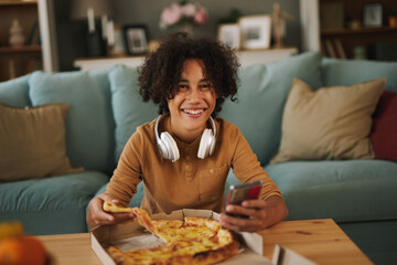 Teenage boy using phone while having pizza at home © Stockphotodirectors