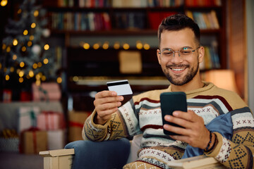 Happy man using credit card and smart phone while buying online at Christmas.