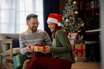Happy couple enjoys in exchanging Christmas presents at home.